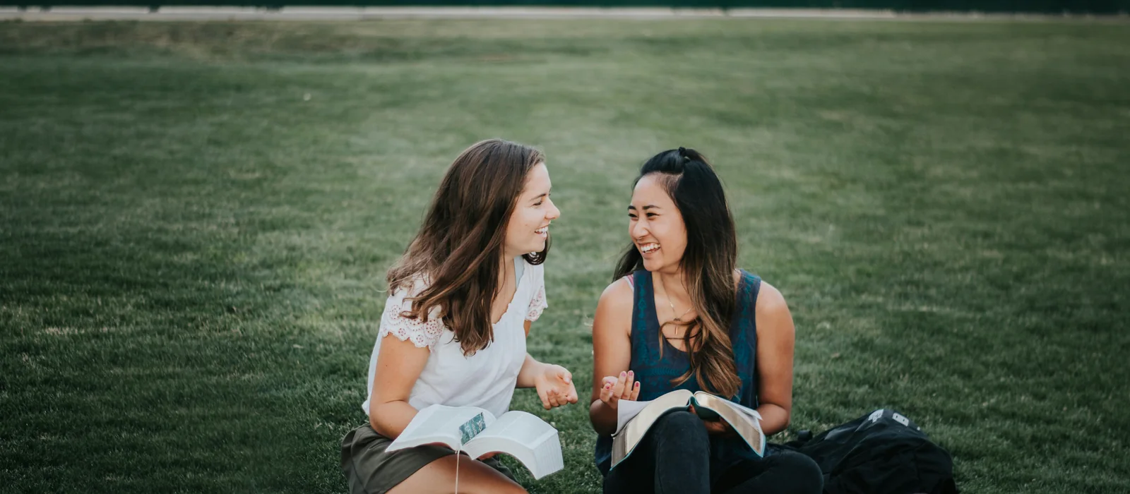 Two friends reading the Bible and talking together outdoors